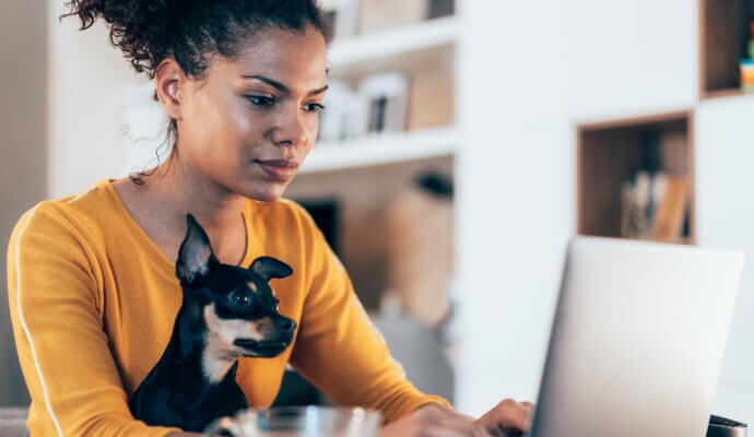 Γυναίκα που χρησιμοποιεί φορητό υπολογιστή ενώ ο σκύλος κάθεται στα γόνατά της