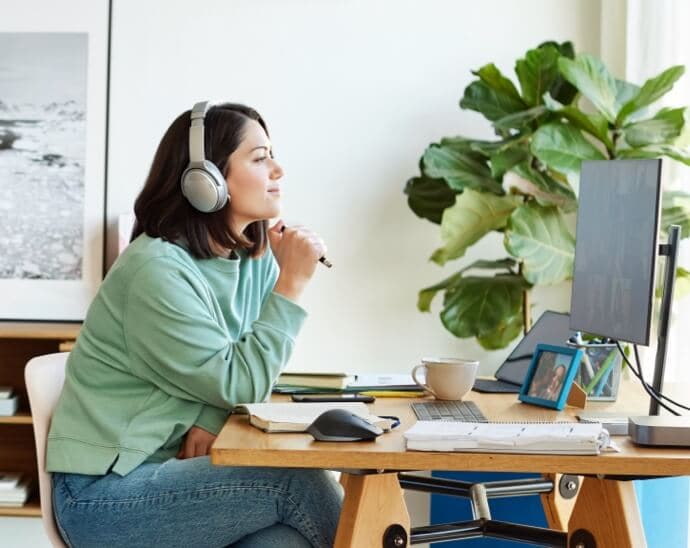 Γυναίκα που φοράει ακουστικά, κρατάει στυλό και κοιτάζει μια οθόνη υπολογιστή