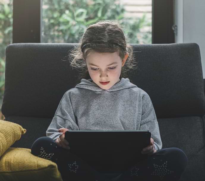 κορίτσι στον καναπέ χρησιμοποιεί φορητό υπολογιστή με ανοιχτό το Norton Family.